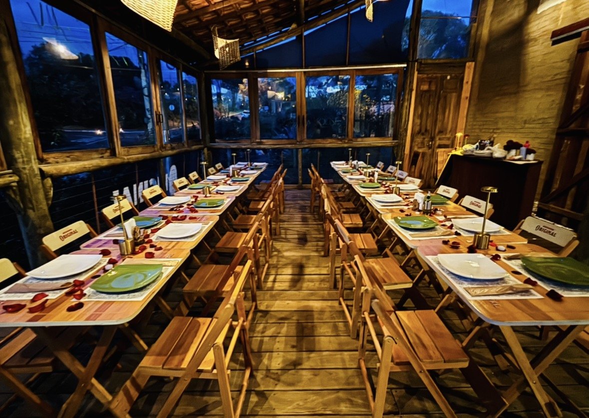 Salão da Pizza House Analândia à noite, com mesas compridas de madeira postas