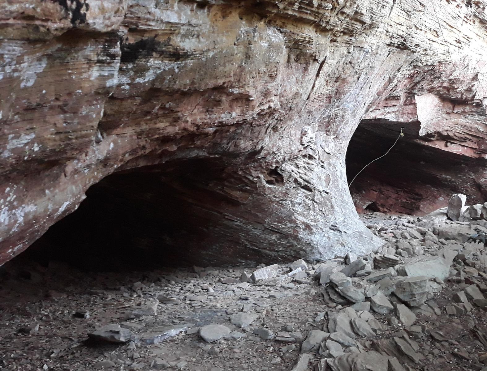 Interior da Gruta Cova da Onça em Analândia (SP), caverna em arenito com aberturas escuras e piso de pedras