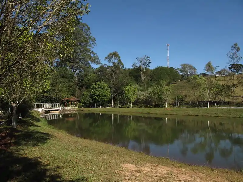 Lago do Recanto da Cascata (Lago da Bruxa) em Analândia (SP), com ponte de madeira, área verde e morros ao fundo