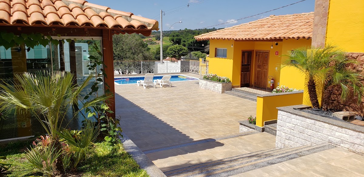 Pátio do Casarão Hostel em Analândia, com construções amarelas, jardim e piscina ao fundo