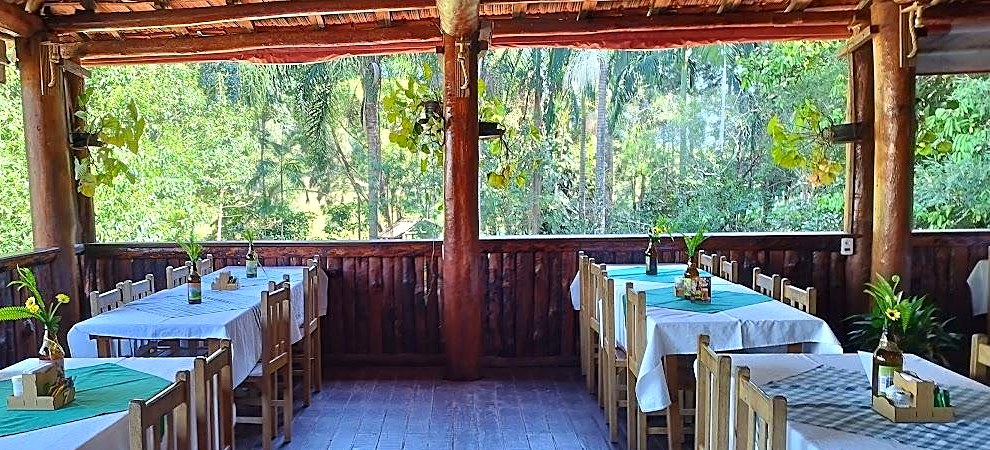 Salão aberto do Restaurante do Morro do Cuscuzeiro em Analândia (SP), mesas com toalhas e vista para a mata