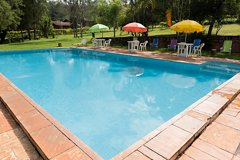 Piscina do Hotel Sopro do Vento em Analândia (SP), com guarda-sóis e cadeiras na área verde